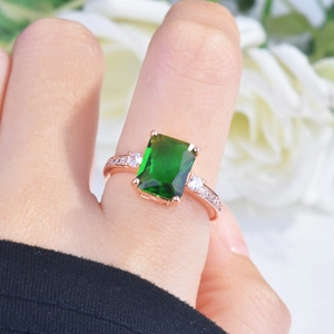 Macro view of emerald-cut green gemstone ring in rose gold finish with zircon accents
