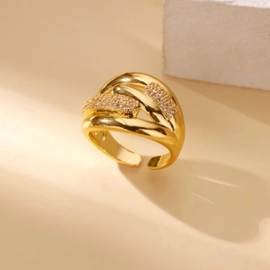 Close-up of golden multi-layered open ring with sparkling zircon stones on beige surface