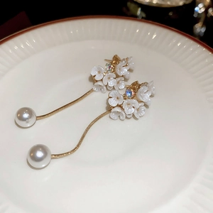 Détail macro de boucles d'oreilles fleurs avec perles et pompons sur plateau blanc