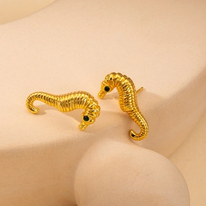 Detailed macro view of gold-plated seahorse earrings with green emerald-colored eyes