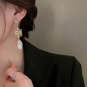 Detail of warm gold Anagram earrings with baroque pearls on a model wearing black suit