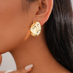 Close-up of golden irregular hammered texture earrings worn by a model in soft lighting