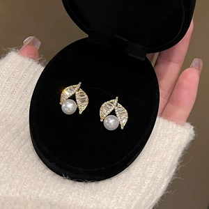 Detailed view of elegant gold leaf pearl earrings with cubic zirconia in a jewelry box