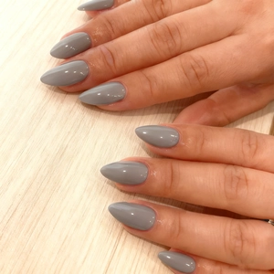 Glossy warm grey almond-shaped press-on nails shown on hands with wooden background
