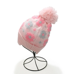 Detail of pink knitted hat featuring floral jacquard pattern and large faux fur pom-pom