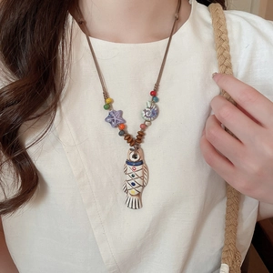 Detailed close-up of a ceramic fish pendant necklace with colorful beads on a linen shirt