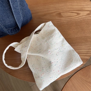 Detailed close-up of cream canvas tote bag with colorful fiber flecks on a wooden surface