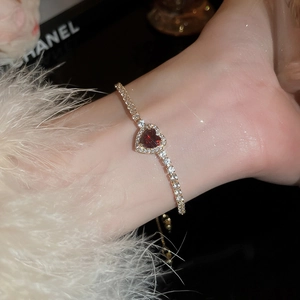 Detail of a gold bracelet featuring a red heart stone and pavé crystal setting