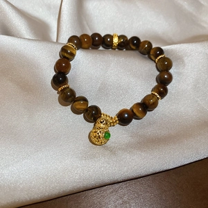 Macro view of tiger eye bead bracelet featuring a hollow gold gourd charm and green accents