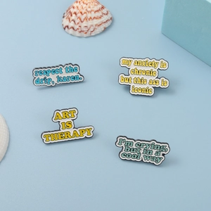 Detailed close-up of four enamel pins with 'Art is Therapy' quotes on blue background