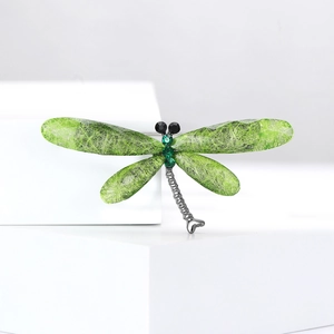 Detailed macro view of dragonfly brooch with green wings and crystal inlay on a stand