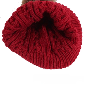 Detail of red cable-knit baby beanie with ribbed cuff and fuzzy pom-pom on white background