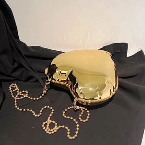 Detailed close-up of a golden heart-shaped hard shell evening bag with beaded metal chain