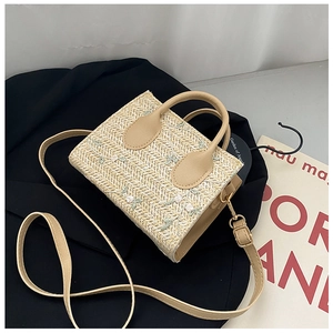 Detail of beige straw handbag with white flower embroidery and brown leather handles