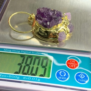 Detailansicht eines natürlichen Amethyst-Anhänger in Katzenpfotenform auf einer Waage