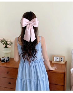 Pink satin bow hair clip worn on long wavy hair in a cozy, elegant indoor setting