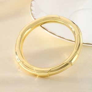 Macro detail of golden hollow cuff bracelet with bamboo texture on beige fabric
