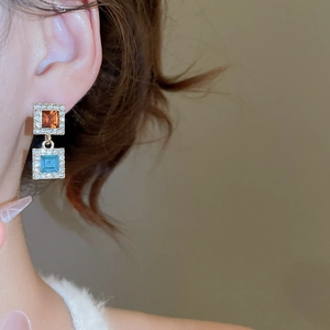 Détail de boucles d'oreilles carrées en cristal ambre et bleu portées par un modèle