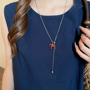 Detail of red pony horse pendant on silver snake chain necklace worn by model