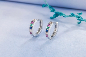 Macro detail of silver hoop earrings featuring a row of vibrant multi-colored gemstones