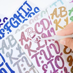 Detail of 1-inch glitter alphabet stickers being applied with tweezers for DIY crafts