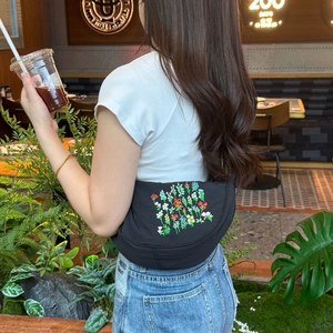 Black canvas dumpling bag with floral embroidery worn by a model in a cafe setting