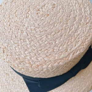Close-up of natural raffia straw hat showing fine hand-woven texture and black ribbon detail