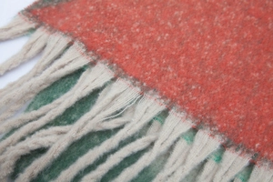 Close-up of thick orange and green jacquard scarf with beige fringe and plush texture