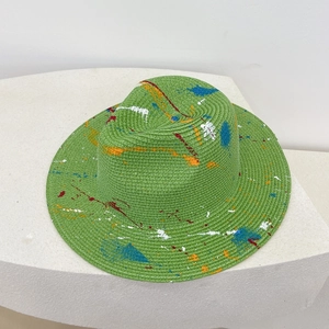 Detail of green straw hat with colorful hand-painted graffiti splatters on a white stand
