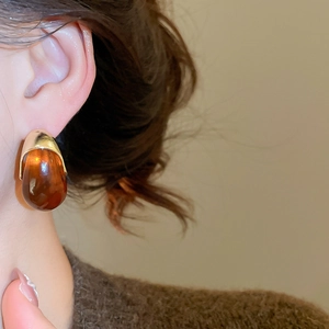 Macro shot of resin C-shaped earring in amber brown with gold metal on model ear