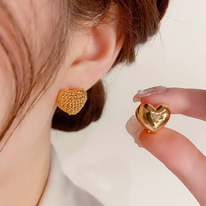 Detail of gold heart earrings showing hollow mesh texture and polished mirror finish