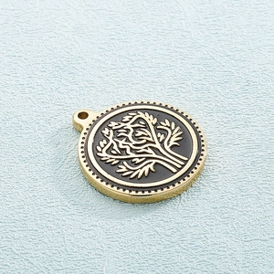 Gold and black stainless steel circular Tree of Life pendant on a blue textured surface