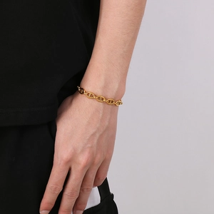 Detailed view of a gold-plated chunky link bracelet worn by a model on a grey background