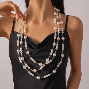 Détail d'un collier à trois rangs de perles et tubes argentés sur une robe en satin noir