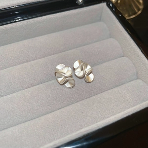 Macro view of matte silver irregular wavy hoop earrings on a grey velvet jewelry box
