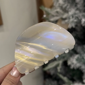 Detail of white acetate hair claw with shell luster texture held in hand by a tree