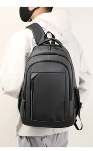 Rear view of a large black waterproof backpack with multiple compartments on a male model