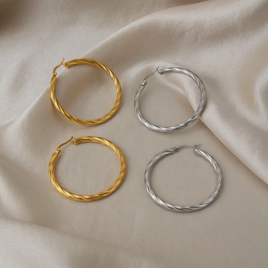 Detailed view of twisted gold and silver hoop earrings on elegant silk background