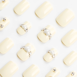 Unghie finte corte quadrate giallo crema con perle a cuore 3D e strass scintillanti