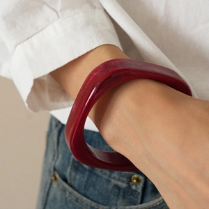 Close-up of deep red resin bangle with translucent marbled texture on model arm