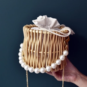Handcrafted woven straw bucket bag with elegant pearl handle and gold chain detail
