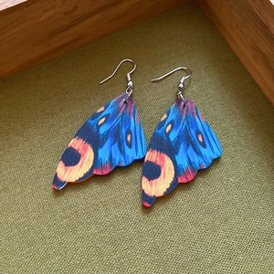 Detail view of blue acrylic butterfly wing earrings with orange eye spots on green fabric