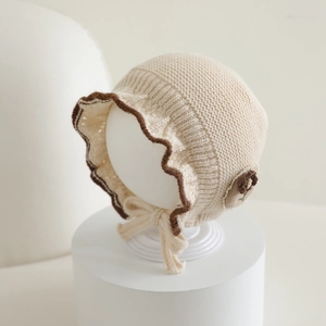 Detail of baby knit hat with brown ruffled edge and cute bear patch on cream cotton