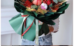 Close-up of Christmas bouquet with red roses, apple, LED lights and festive wrapping