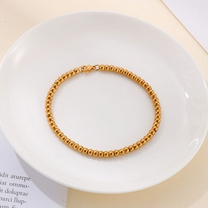 Top view of gold beaded stainless steel bracelet with lobster clasp on a white plate