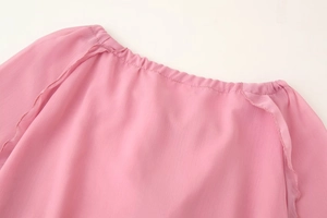 Détail d'une robe en mousseline rose montrant le décolleté en V plissé et le tissu