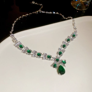 Macro shot of silver necklace with square clear stones and a pear-shaped green gemstone