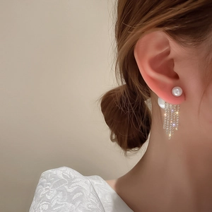 Close-up of elegant pearl and rhinestone tassel earrings worn by a model in soft light