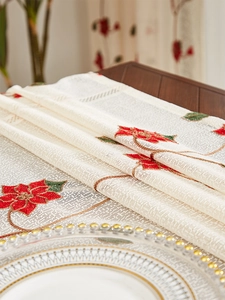 Detail of red poinsettia embroidery on beige lace tablecloth for Christmas decor