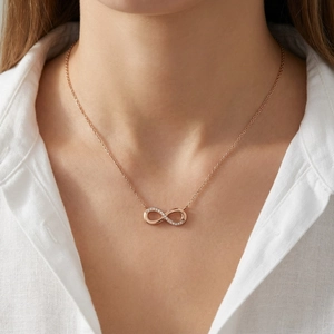 Close-up of a rose gold infinity necklace with small diamonds on a model's neckline